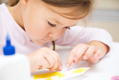 Cute little girl applying a color paper using glue while doing arts and crafts in preschool